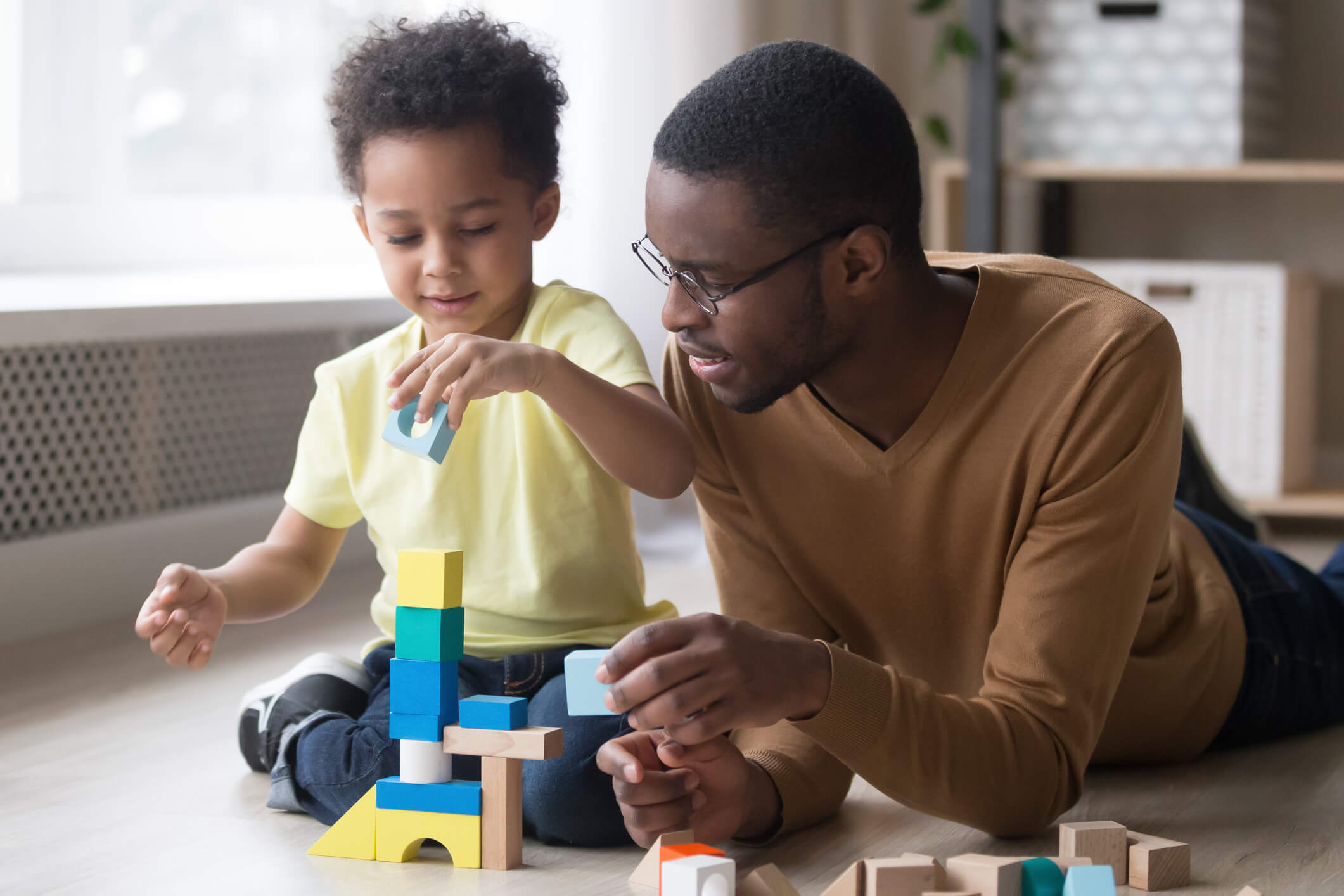 African father and son play with colourful toy blocks