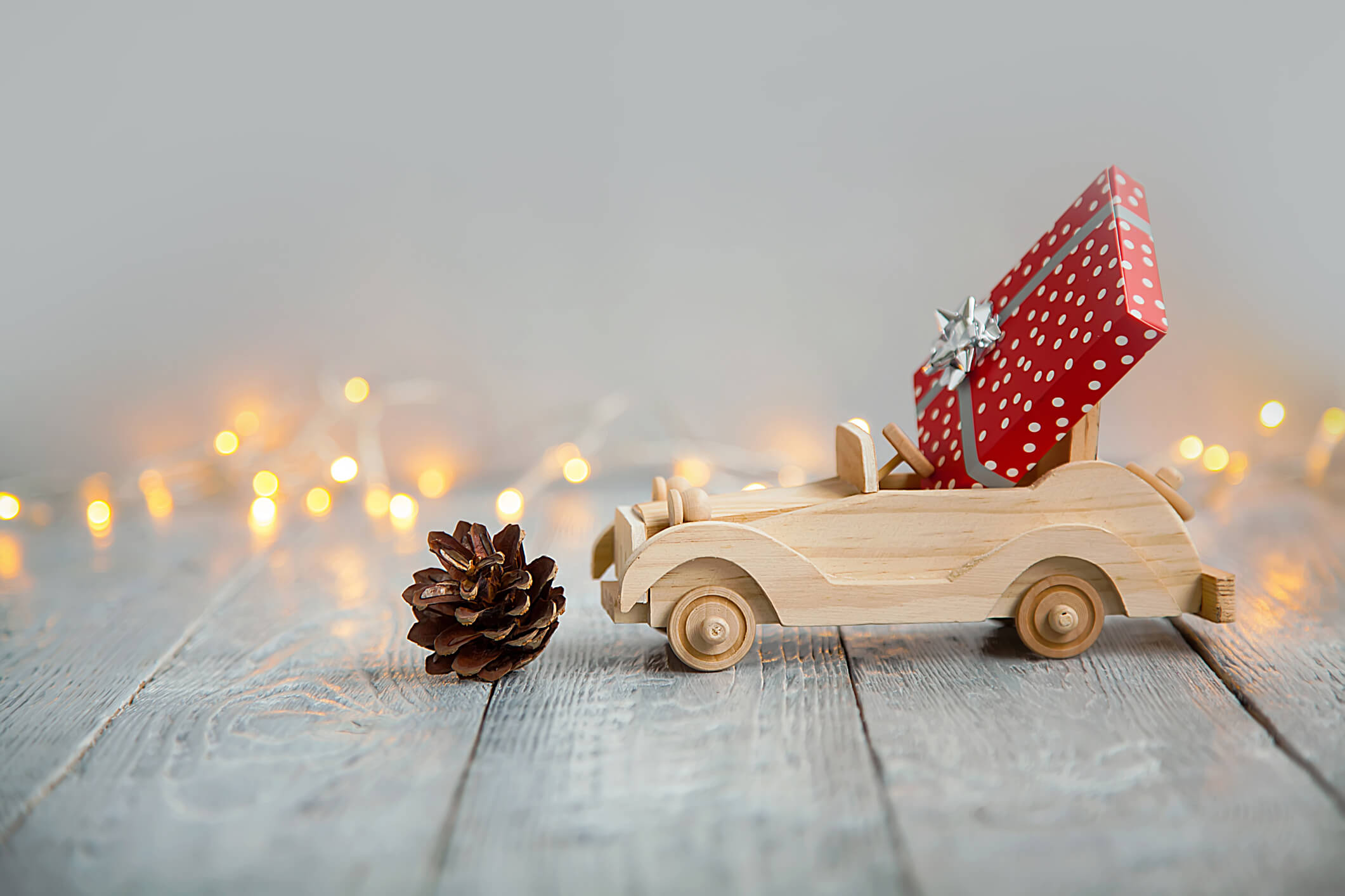 wooden car with gift on a wooden gray background and lights from the garland. Christmas concept