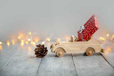wooden car with gift on a wooden gray background and lights from the garland. Christmas concept