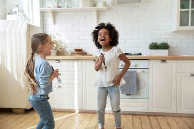 Happy little multiethnic girls sing in kitchen together