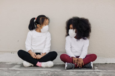 Beautiful young girls sitting chatting whilst wearing protective face masks