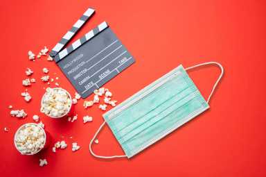 Movie clapperboard, pop corn and protective medical mask against red background