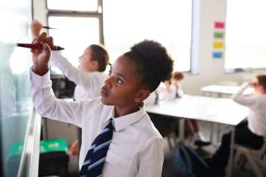 Female High School Students Wearing Uniform Using Interactive Whiteboard During Lesson