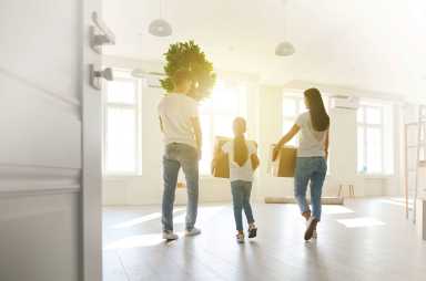 Happy family with children moving with boxes in a new apartment house. Back view.