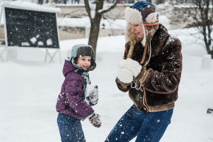 A child and woman, wearing heavy winter clothes, playing together in the snow over mid-winter break