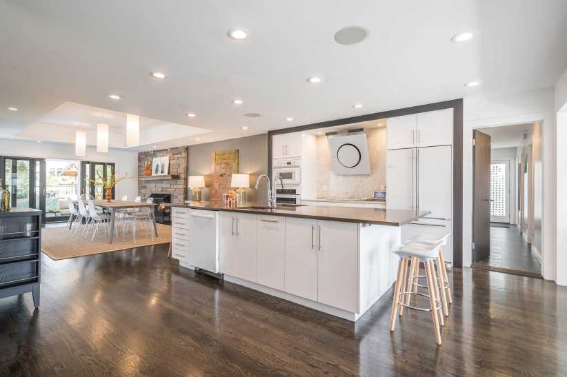 Bright open-concept kitchen and dining area with white cabinetry, large island, dark wood floors, and modern lighting fixtures.