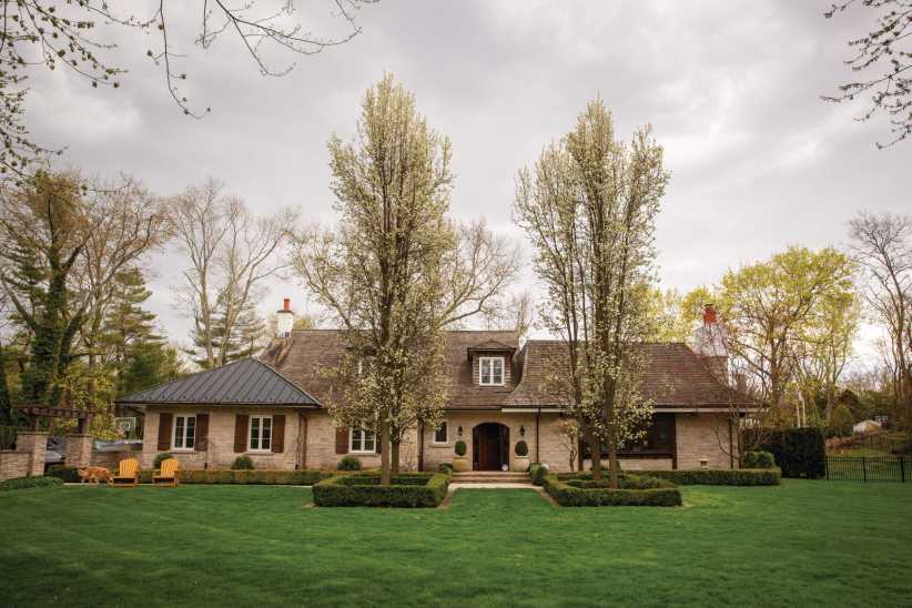 Elegant two-story suburban home with brick & siding exterior, symmetrical windows, manicured lawn, large front porch under soft daylight.