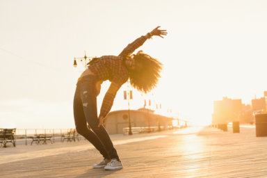 Young woman bending backwards on pier at sunset, Coney Island, New York, USA