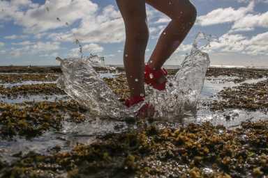 Child in rubber red sandals jumping up and down and splashing the water