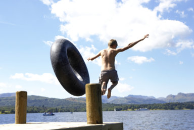 Boy (11-13) leaping from lake jetty with rubber ring, rear view