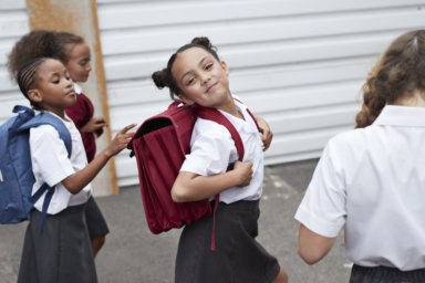 Cute schoolgirl looking to camera while walking from school with friends