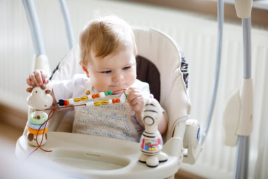 Cute adorable newborn baby girl sitting in swing indoors