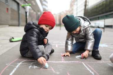 2 children drawing with a chalk stick in the street