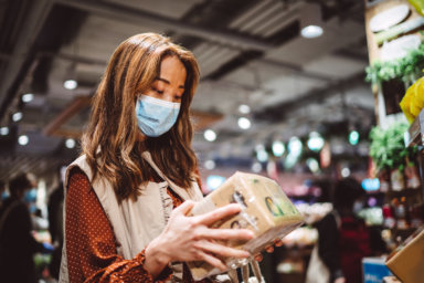 Pretty young lady with medical face mask shopping joyfully in supermarket