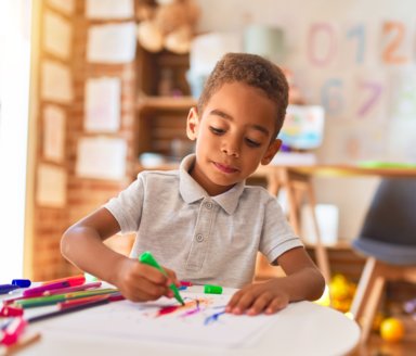 Beautiful african american toddler drawing using paper and marker pen at kindergarten