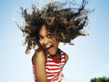 Girl (10-12) wearing earphones, outdoors, smiling, portrait