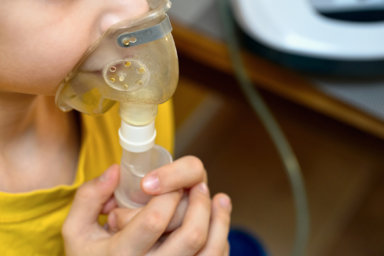 Child makes inhalation at home with nebulizer on out of focus background. Example of combating respiratory diseases such as tracheitis bronchitis pneumonia with medical equipment at home conditions.