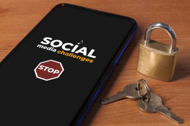 Smartphone showing the message “stop social media challenges” a wooden table with a lock and keys.