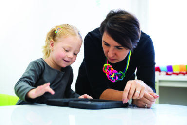 Toddler girl in child occupational therapy session doing playful exercises on a digital tablet with her therapist.