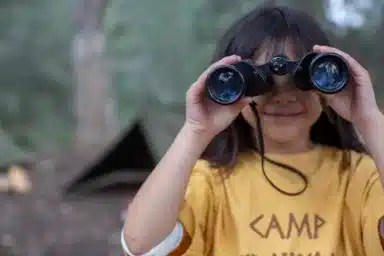 Portrait cute girl bird watching at summer camp with binoculars