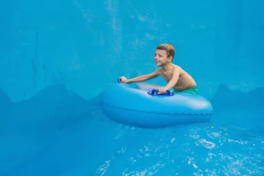 Boy on a pool float on artificial waves in a water park