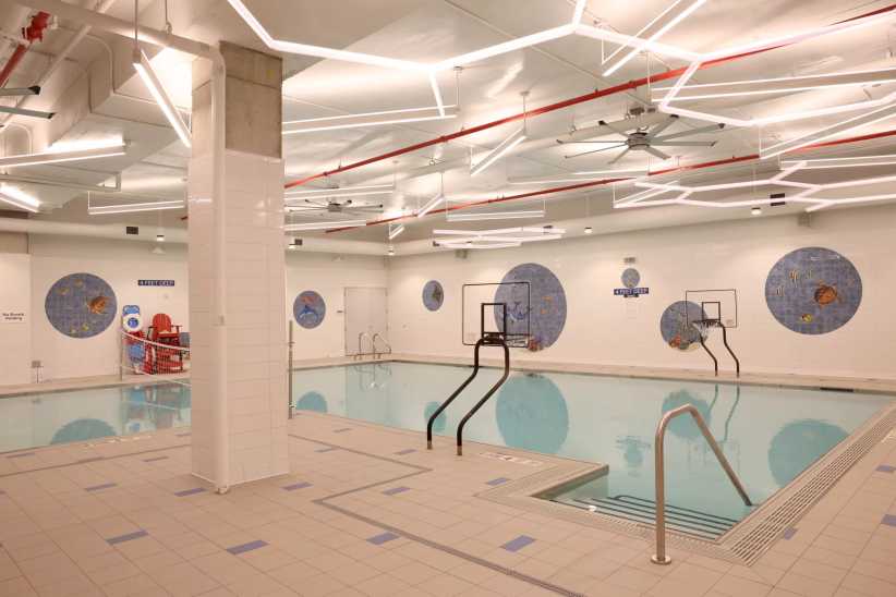 An indoor swimming pool with basketball hoops, modern lighting, and decorative wall murals, located at Chelsea Piers Field House in Brooklyn.
