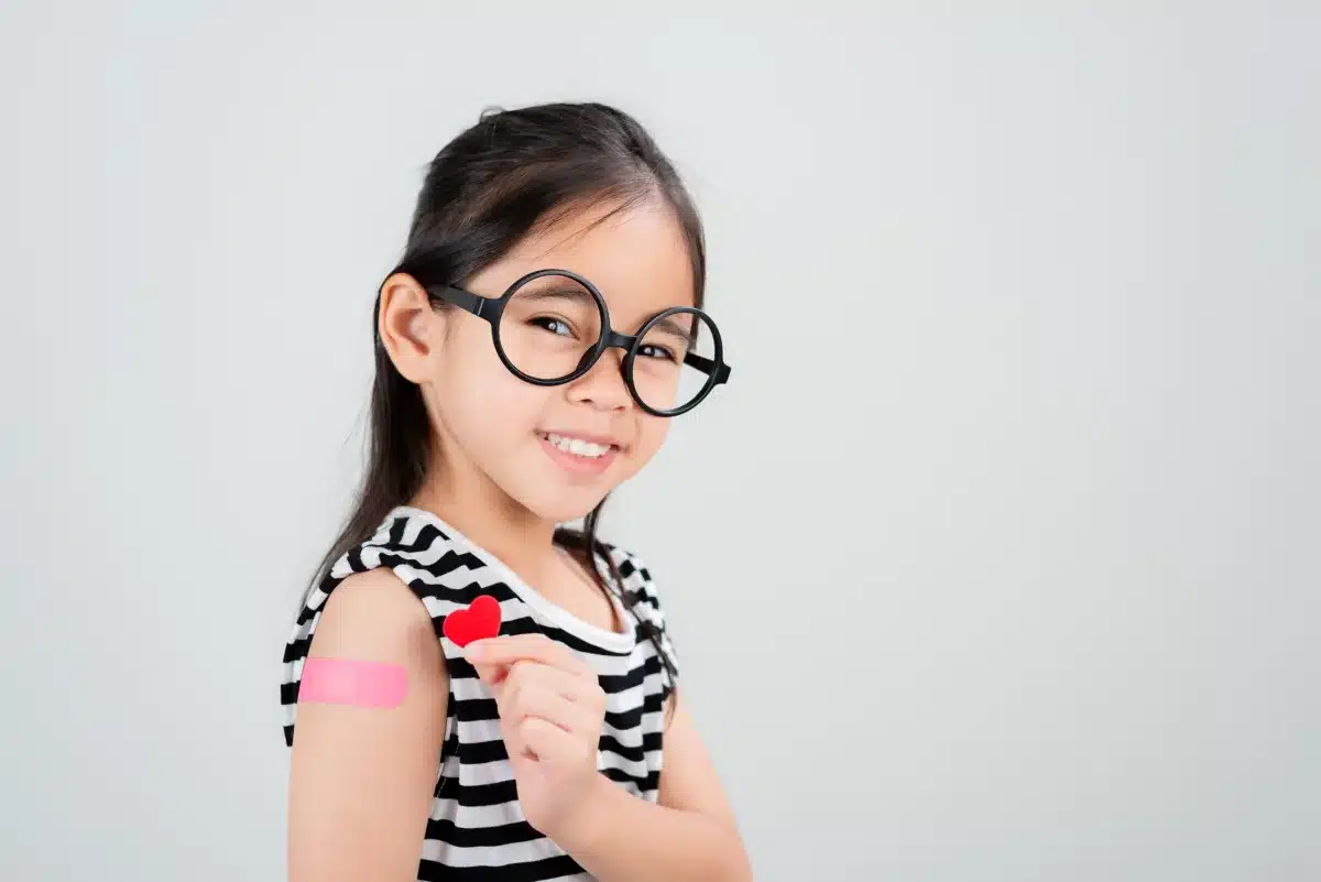 Asian little girl wear glasses showing her arm with bandage after virus vaccine happy Kid and child vaccination campaign. Protect your kid with vaccine concept