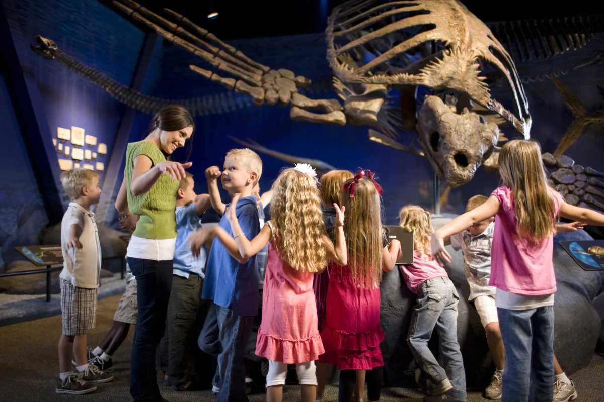 Children on a field trip at NYC natural history museum, learning about dinosaur fossils with teacher
