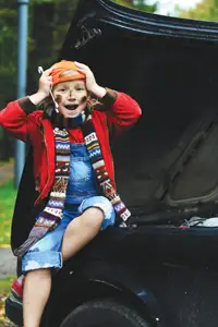 little girl in dirty clothes sitting on car holding mechanic tools