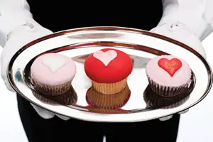 three cupcakes with heart shaped icing on a silver platter