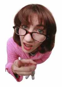 A woman with glasses and a pink shirt leans forward, pointing her finger directly at the camera with a stern expression.