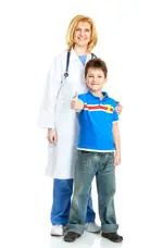 A female doctor in a white coat stands behind a young boy in a blue polo shirt who is giving a thumbs-up.
