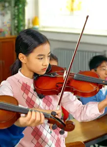 young girl playing a violin; child in music class; after-school activities