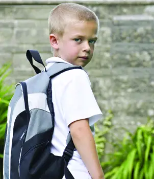 back to school anxiety; worried boy carrying a backpack, on his first day of school