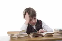 Young boy reading a books at a desk looking frustrated.