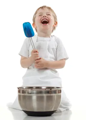 child laughing while holding spatula, baking brownies; kid cooking in kitchen