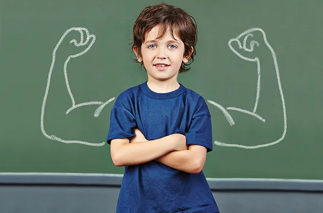 child with muscles drawn on blackboard behind him