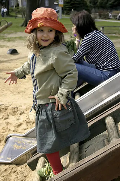 child on playground with nanny in background