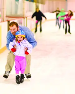 dad helping young daughter ice skate; ice skating rink