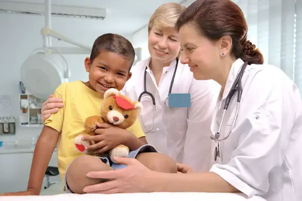 Two female doctors with boy holding a teddy bear