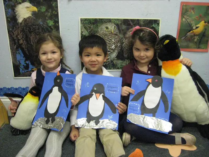 children holding construction paper penguins