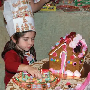 little girl decorating a gingerbread house for the holidays