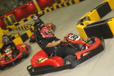 Drivers in helmets and racing gear navigate red go-karts around a track lined with yellow and black barriers.