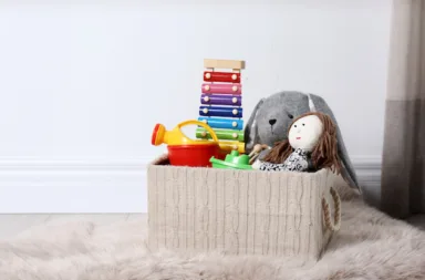Box,With,Different,Child,Toys,On,Floor,Against,White,Wall.