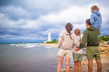 Family,Of,Four,Near,Stormy,Sea,Coast,Look,At,Lighthouse