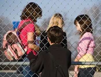 child on outside of playground looking in; kids separated by a fence