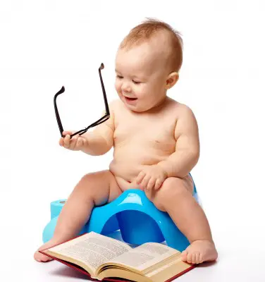 baby sitting on training potty holding glasses with book