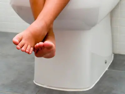 Cropped photo of a child's dangling feet, sitting on toilet