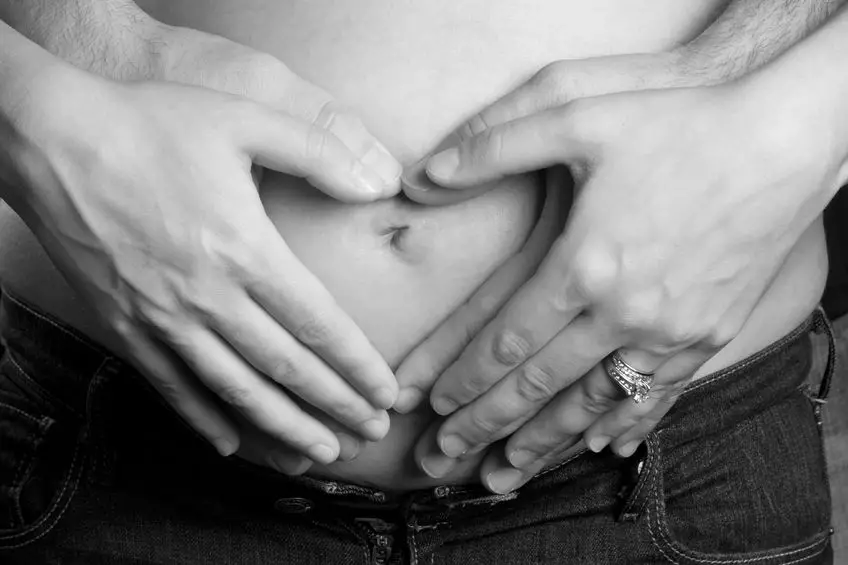 pregnant woman holding stomach with man's arms around her belly