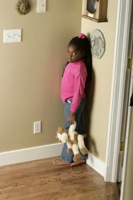 little girl standing in the corner of the room holding stuffed animal